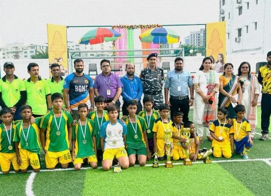 Student sports team in green and yellow jerseys posing with trophies, medals, officials, and teachers on turf ground