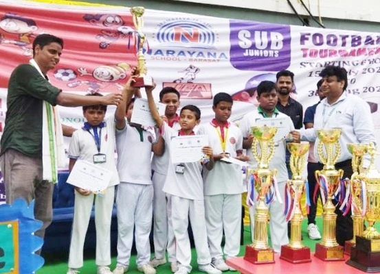 Coach and student football players in white uniforms holding winner trophy and merit certificates in front of tournament banner