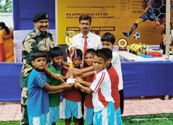 Officer in uniform and teacher presenting championship trophy to junior football players holding it together